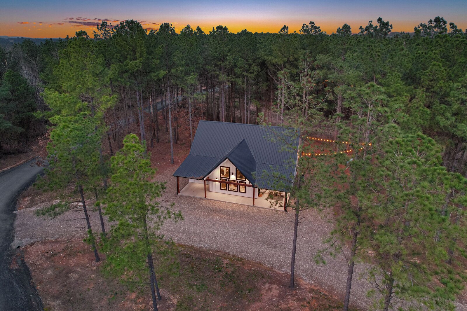 House surrounded by forest with gravel driveway and metal roof