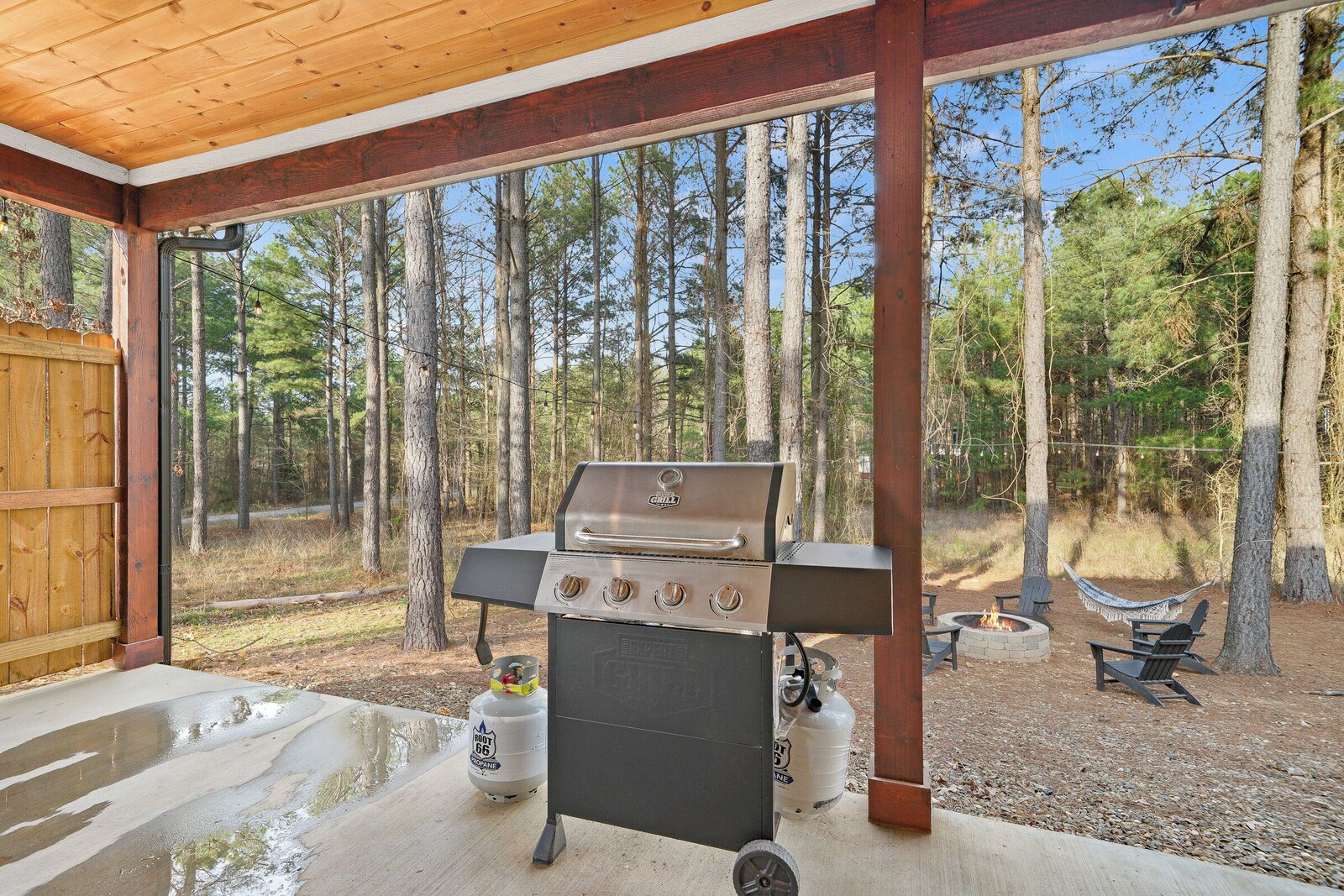 Outdoor patio with grill, fire pit, and seating surrounded by trees
