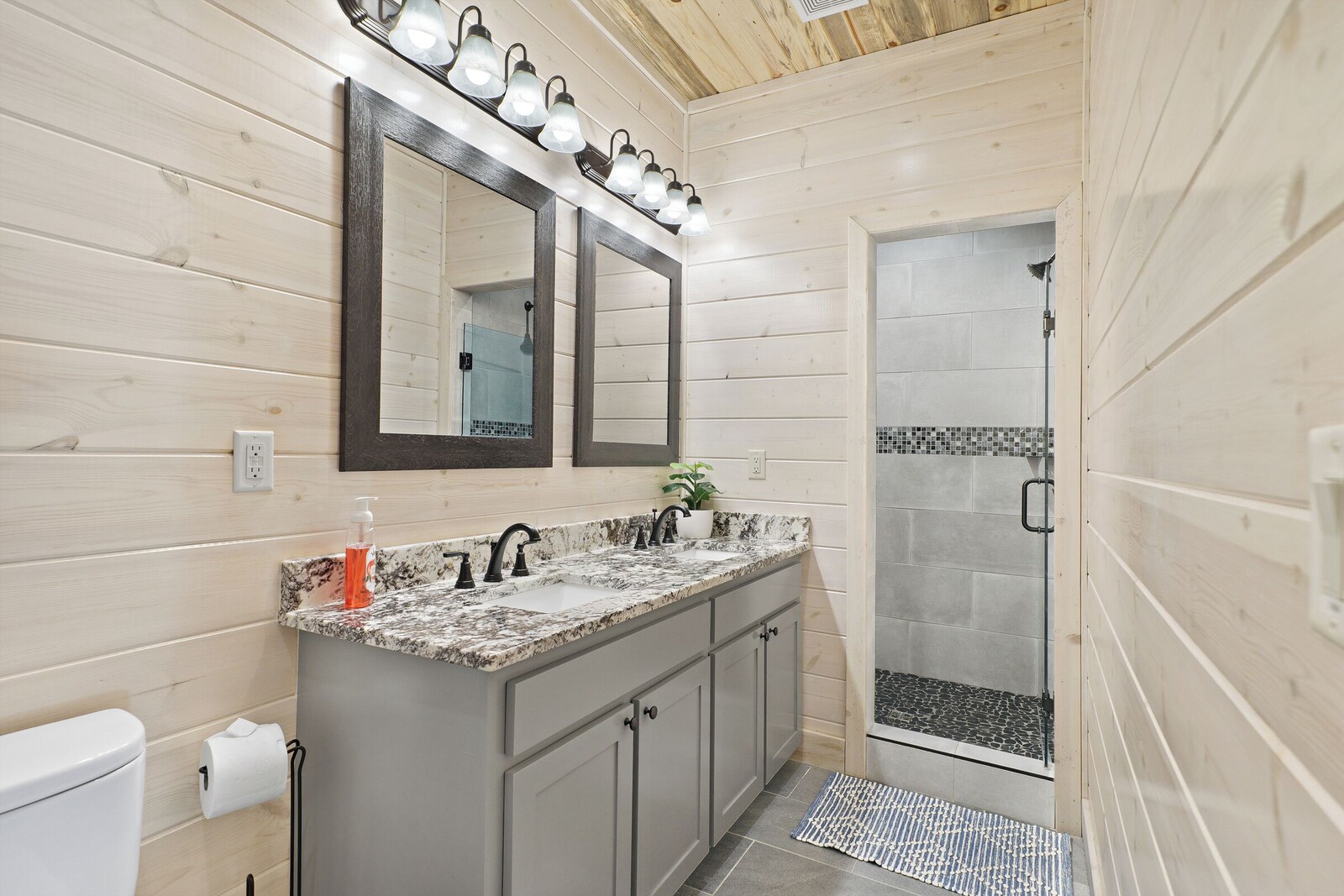 Bathroom with wooden paneling, marble sink, and glass shower