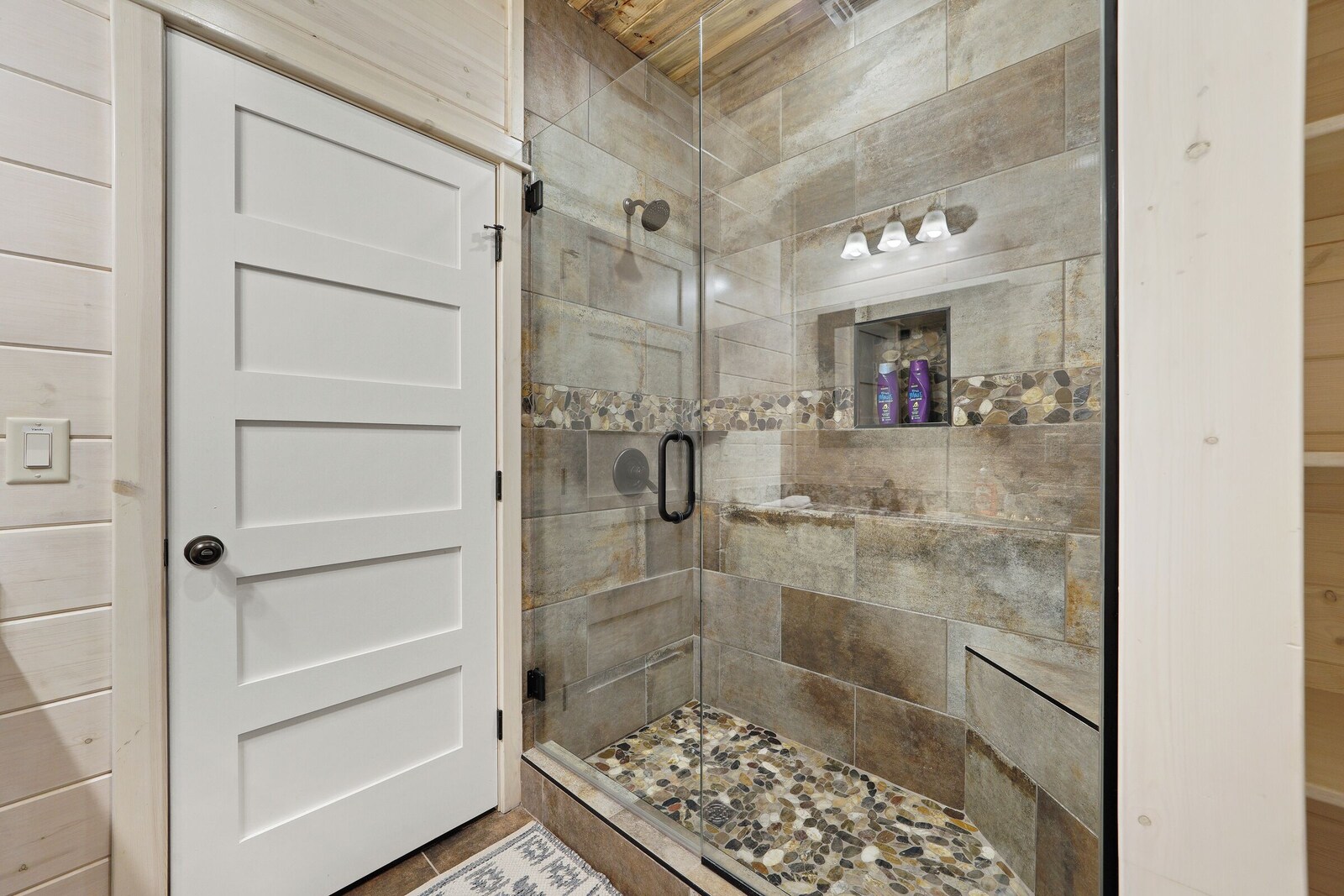 Walk-in shower with stone tile and toiletries shelf