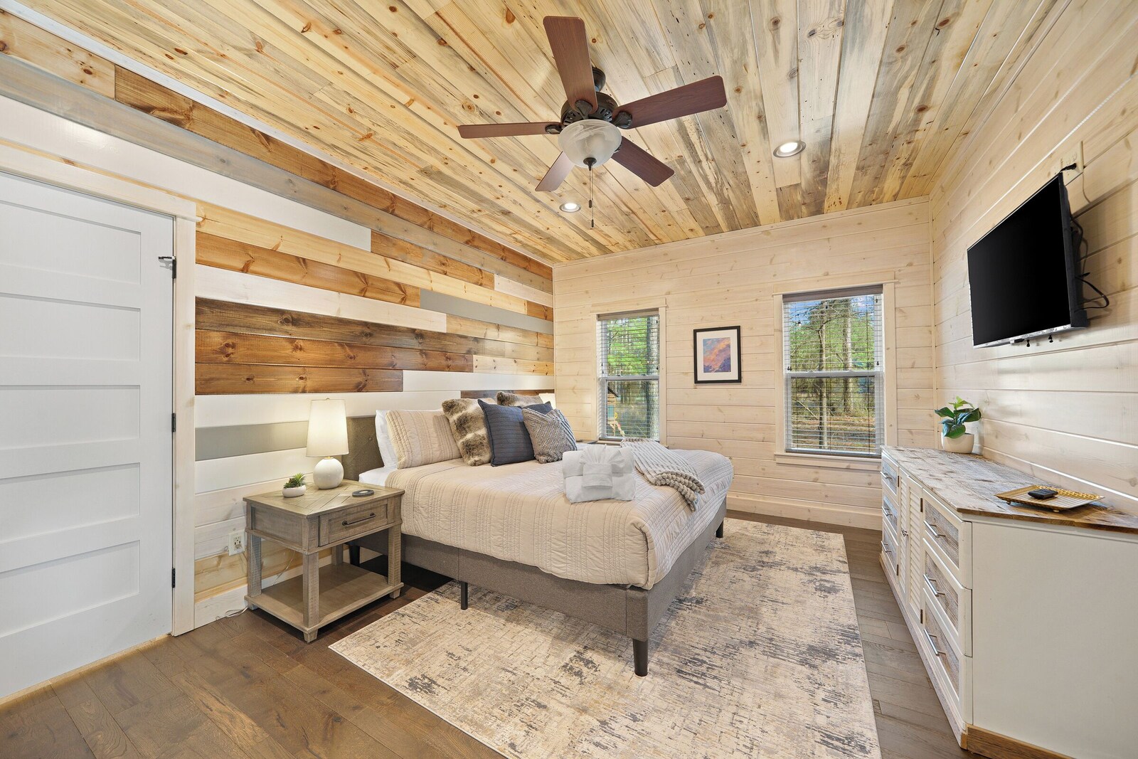 Bedroom with wooden ceiling, white bedding, dresser, and mounted TV